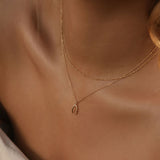A close-up of a light-skinned woman in off-shoulder cream fabric wearing the LLUME Jewelry Wishbone Daily Set—a delicate gold necklace set featuring a small Wishbone Necklace pendant—captured in soft, warm lighting.