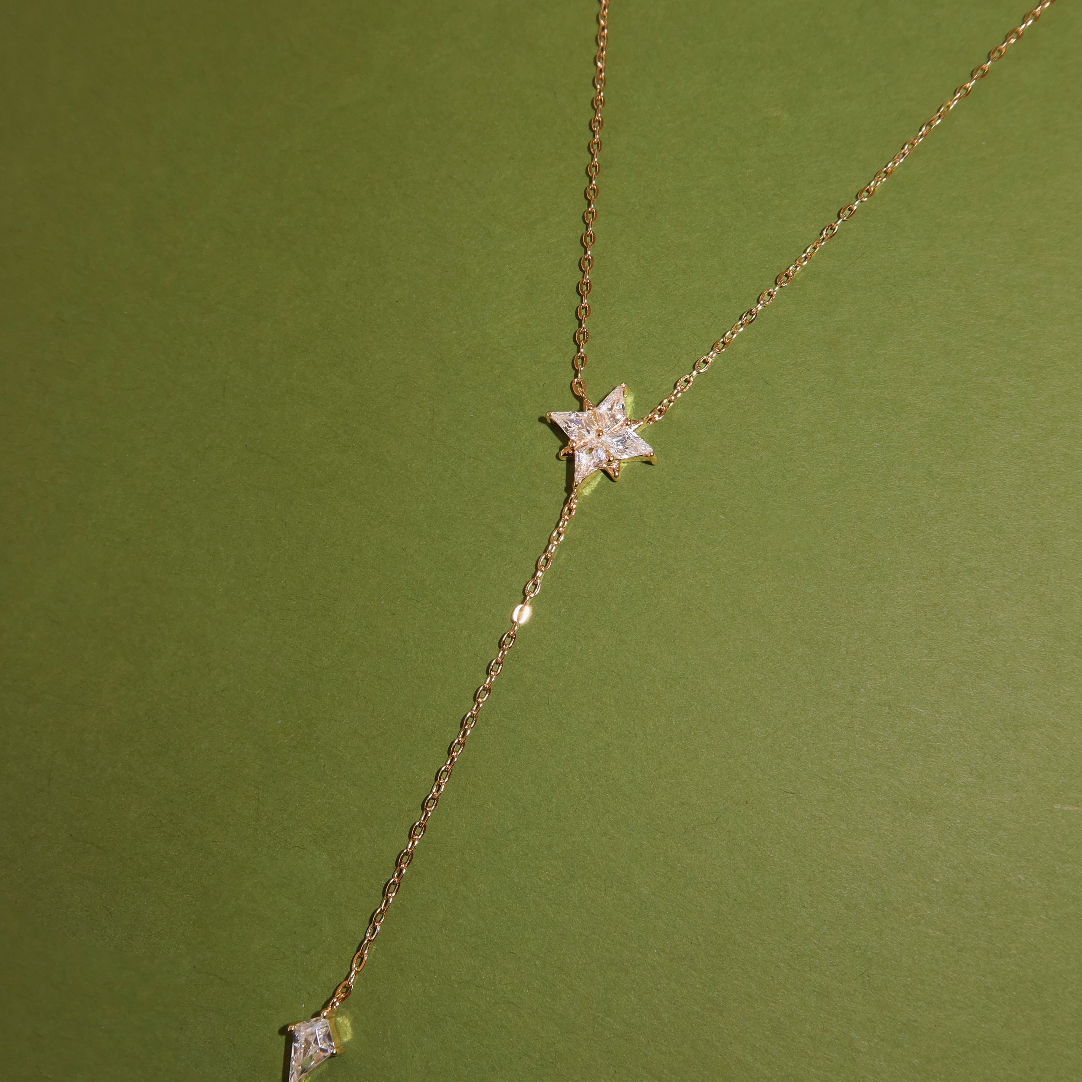 The Starlit Necklace by LLUME Jewelry is a waterproof gold lariat featuring a star-shaped pendant and a small kite-shaped drop.