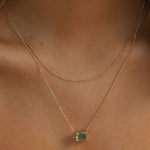 A close-up of a woman’s neck wearing the Seafoam Daily Set by LLUME Jewelry: one delicate gold chain is plain, while the other showcases a rectangular green gemstone pendant, capturing effortless coastal elegance.