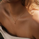 A close-up shows a woman in an off-the-shoulder light top, her wavy blonde hair to one side, elegantly wearing the Wishbone Daily Set by LLUME Jewelry.