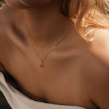 A close-up shows a woman in an off-the-shoulder light top, her wavy blonde hair to one side, elegantly wearing the Wishbone Daily Set by LLUME Jewelry.