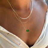 A person wearing the LLUME Jewelry Seagrass Favorites Set—three layered necklaces including a flat chain, a paperclip chain, and a chain with a rectangular green gemstone pendant—all styled over a white, slightly torn top.
