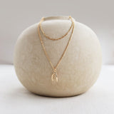 A round, off-white ceramic vase displays the LLUME Jewelry Wishbone Daily Set—featuring the Colette Necklace and Wishbone Necklace—elegantly arranged against a neutral background.