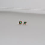 LLUME Jewelry’s Destiny Earrings in gold feature emerald green studs encircled by small clear stones, shown on a plain light gray background.