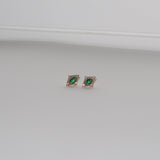 LLUME Jewelry’s Destiny Earrings in gold feature emerald green studs encircled by small clear stones, shown on a plain light gray background.