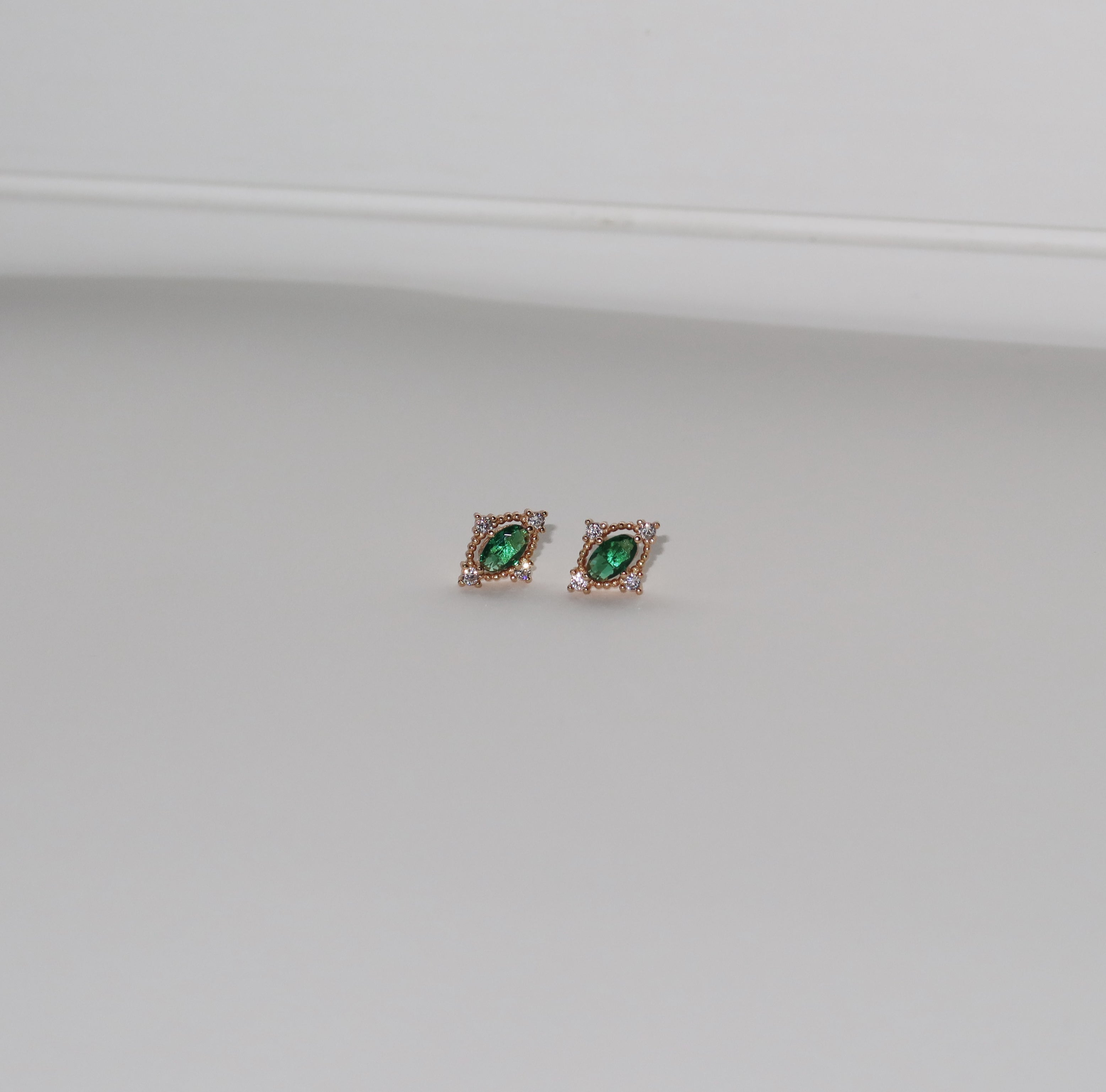 LLUME Jewelry’s Destiny Earrings in gold feature emerald green studs encircled by small clear stones, shown on a plain light gray background.