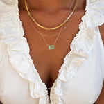 Close-up of someone wearing LLUME Jewelry's Seafoam Favorites Set: a white ruffled top paired with layered necklaces featuring a paperclip chain, skinny hailey chain, and a rectangular seafoam glass pendant.