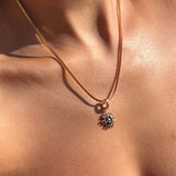 A close-up of LLUME Jewelry's Every Occasion Set shows a gold sun-shaped charm necklace with a snake chain resting on bare skin, its warm shine beautifully highlighted by the sunlight.
