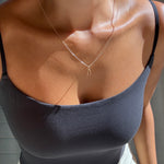 Wearing a black tank top, the person showcases LLUME Jewelry's Wishbone Necklace on a layered chain, sunlight highlighting their skin from shoulders to waist.