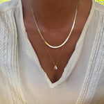 Adorned in a white blouse with lace accents, a person elegantly showcases the LLUME Jewelry Elara Classics Set—featuring two gold necklaces, including a skinny Hailey chain and a solitaire teardrop pendant—demonstrating the art of thoughtfully layered jewelry.