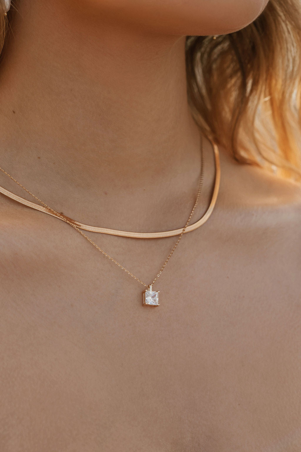 A close-up of a woman’s neck wearing LLUME Jewelry’s Vacation Capsule Set: one sleek chain and one delicate chain with a square stone pendant—perfect for stacking and elevating any jewelry look.