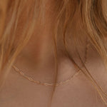 Close-up of a woman's neck with wavy, light brown hair wearing the Adelene Paperclip Chain by LLUME Jewelry—an 18k gold plated necklace with small, elongated links.