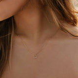 A close-up of a woman's neck wearing the LLUME Jewelry Whisper Necklace—a gold-plated sterling silver piece with a small rectangular pendant—against her light skin, white off-shoulder top, and partially visible loose hair.