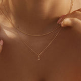 A close-up of a woman wearing the LLUME Jewelry Whisper Daily Set—two delicate gold necklaces, one with a subtle pendant—against bare skin and a white strapless top. Her hands gently touch the chains, highlighting timeless everyday style.