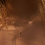 Close-up of a neck wearing LLUME Jewelry's Whisper Daily Set—two delicate gold chain necklaces—in warm, natural light. Strands of light brown hair frame this perfect everyday accessory.