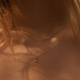 Close-up of a neck wearing LLUME Jewelry's Whisper Daily Set—two delicate gold chain necklaces—in warm, natural light. Strands of light brown hair frame this perfect everyday accessory.