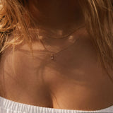 Close-up of a woman with long blonde hair in an off-shoulder white top wearing the LLUME Jewelry Whisper Daily Set—two delicate gold necklaces, including a small vertical Whisper pendant—perfect for everyday wear.