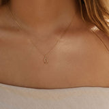 A woman wears the Wishbone Necklace by LLUME Jewelry, featuring a delicate wishbone pendant; her wavy hair and light off-shoulder top showcase this versatile accessory.