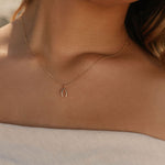 A woman exudes timeless elegance in an off-the-shoulder light top, highlighted by the LLUME Jewelry Wishbone Necklace, its delicate gold charm softly illuminated by natural light.