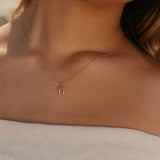A woman exudes timeless elegance in an off-the-shoulder light top, highlighted by the LLUME Jewelry Wishbone Necklace, its delicate gold charm softly illuminated by natural light.