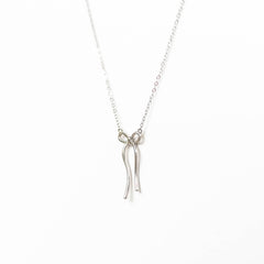 The Bow Necklace by LLUME Jewelry is a limited edition silver piece with a fine chain and minimalist bow pendant, showcased on a plain white background.