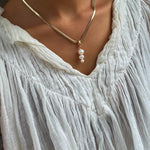 Wearing a crinkled white v-neck blouse, a person accessorizes with the LLUME Jewelry Every Occasion Set—a gold snake chain necklace adorned with four dangling white pearls.