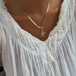 A person wearing a white, textured V-neck blouse and the Every Occasion Set by LLUME Jewelry, featuring a gold charm necklace with a starfish pendant.