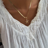 A person wearing a white, textured V-neck blouse and the Every Occasion Set by LLUME Jewelry, featuring a gold charm necklace with a starfish pendant.
