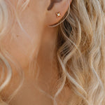 Close-up of a person's ear with wavy blonde hair, wearing LLUME Jewelry's Myra Studs—small gold star-shaped earrings that make an elegant addition to any jewelry collection.