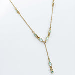 The Ever Necklace by LLUME Jewelry is a gold lariat with a Y-shaped drop, adorned with small pear and round blue cubic zirconia stones along the chain and drop, shown on a white background.