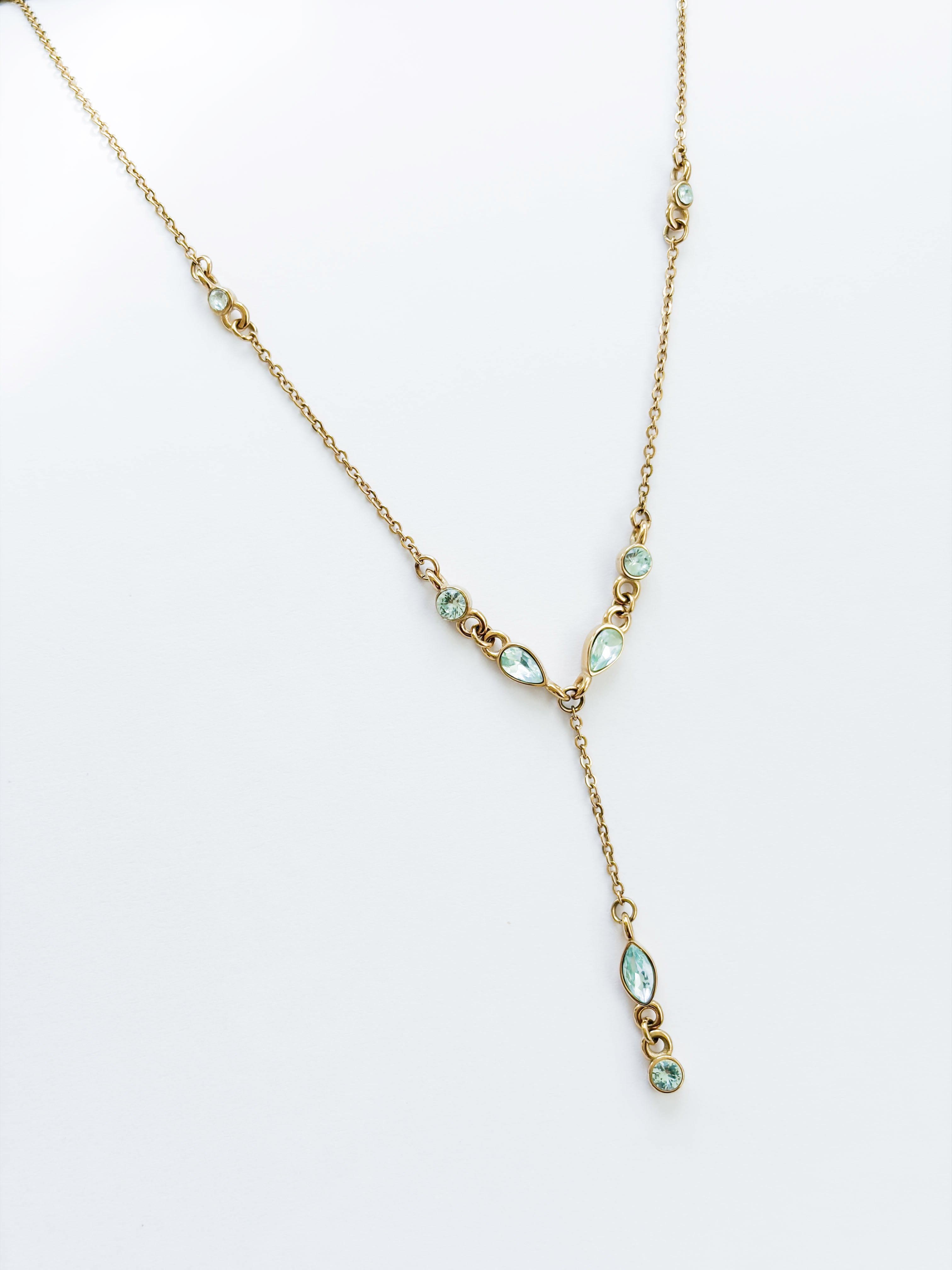The Ever Necklace by LLUME Jewelry is a gold lariat with a Y-shaped drop, adorned with small pear and round blue cubic zirconia stones along the chain and drop, shown on a white background.