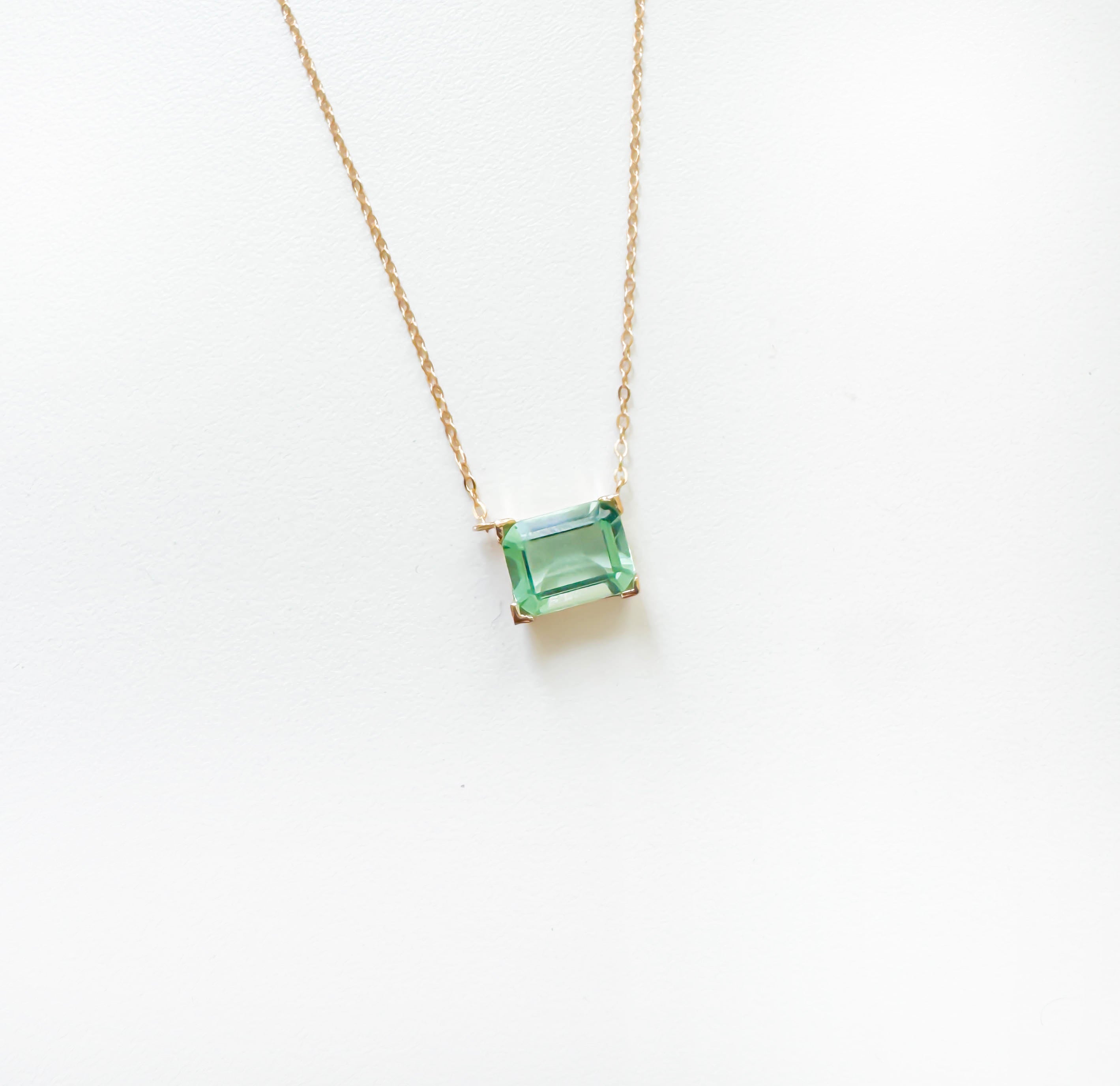 The LLUME Jewelry Seafoam Glass Necklace features a gold chain with a square-cut green gemstone pendant, capturing coastal magic and elegantly displayed on a white background.