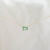 The Seafoam Glass Necklace by LLUME Jewelry features a delicate gold chain and a small rectangular green pendant, evoking coastal magic against a soft, light background.