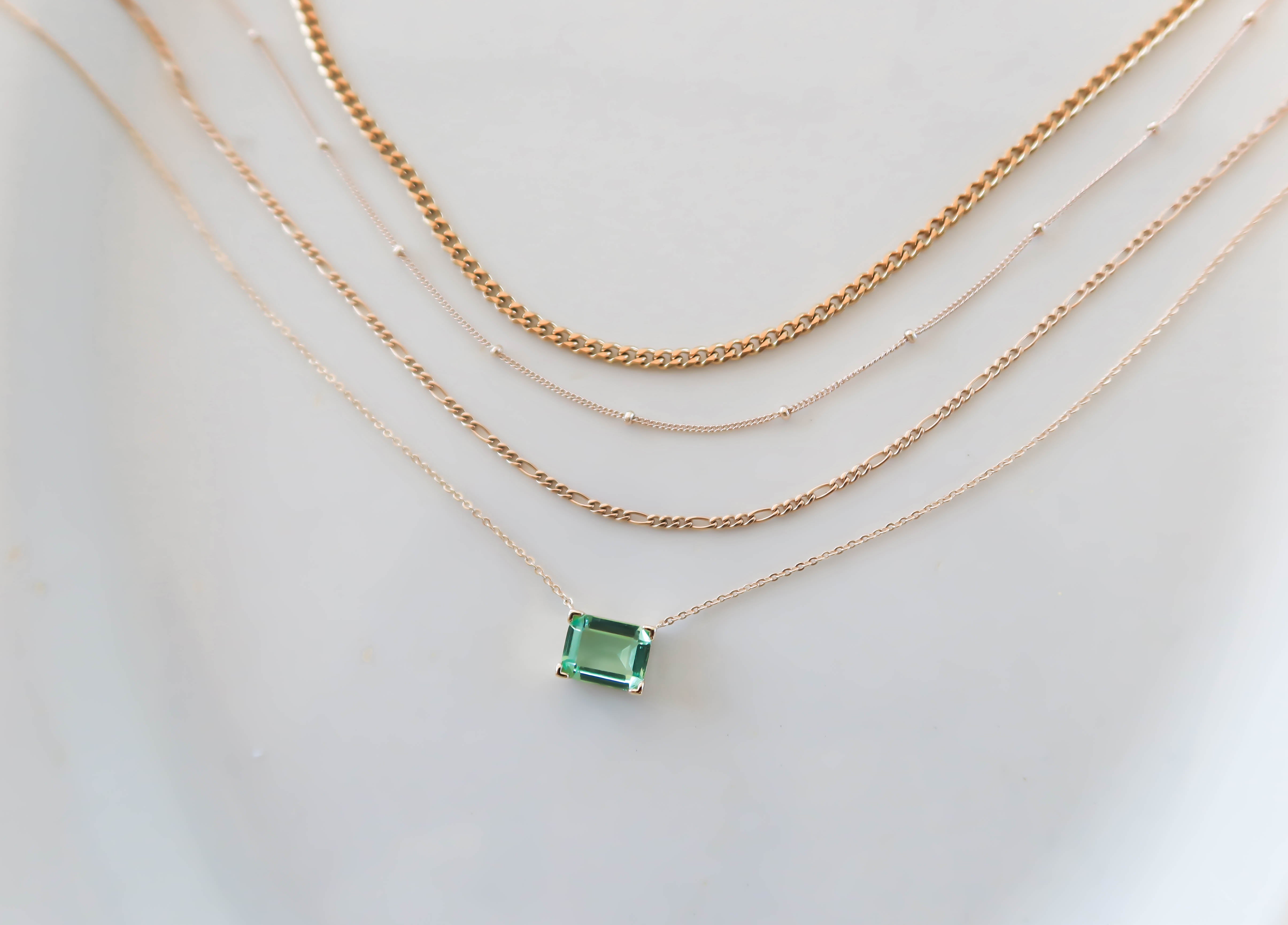Four layered gold necklaces, the shortest featuring a rectangular Seafoam Solstice pendant.