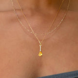 A person wears the LLUME Jewelry Sunspill Daily Set, featuring a necklace with a yellow teardrop pendant and small stone accents, paired with a grey strapless top.