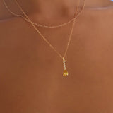 A close-up of a person’s neck wearing LLUME Jewelry’s Sunspill Daily Set—two delicate gold chains, one with a small yellow pendant—set against a blurred outdoor background.