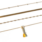 Four gold necklaces from the LLUME Jewelry Sunspill Solstice Set are displayed in parallel on a white background; one features a yellow teardrop-shaped pendant.