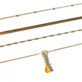 Four gold necklaces from the LLUME Jewelry Sunspill Solstice Set are displayed in parallel on a white background; one features a yellow teardrop-shaped pendant.