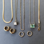 The Vacation Capsule Set by LLUME Jewelry features gold chains with distinctive pendants and chic gold earrings, elegantly displayed on a gray background—your go-to summer jewelry collection.
