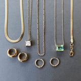 The Vacation Capsule Set by LLUME Jewelry features gold chains with distinctive pendants and chic gold earrings, elegantly displayed on a gray background—your go-to summer jewelry collection.