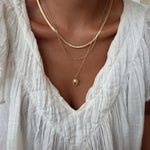 A person wearing a white textured blouse and the LLUME Jewelry Vintage Favorites Set—featuring three layered gold necklaces—shown from the shoulders to the chest.