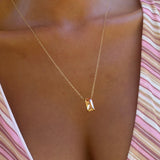 A close-up of the Wild Honey Necklace by LLUME Jewelry, a dainty gold necklace with a rectangular pendant, worn by a person in a pink and white striped top.