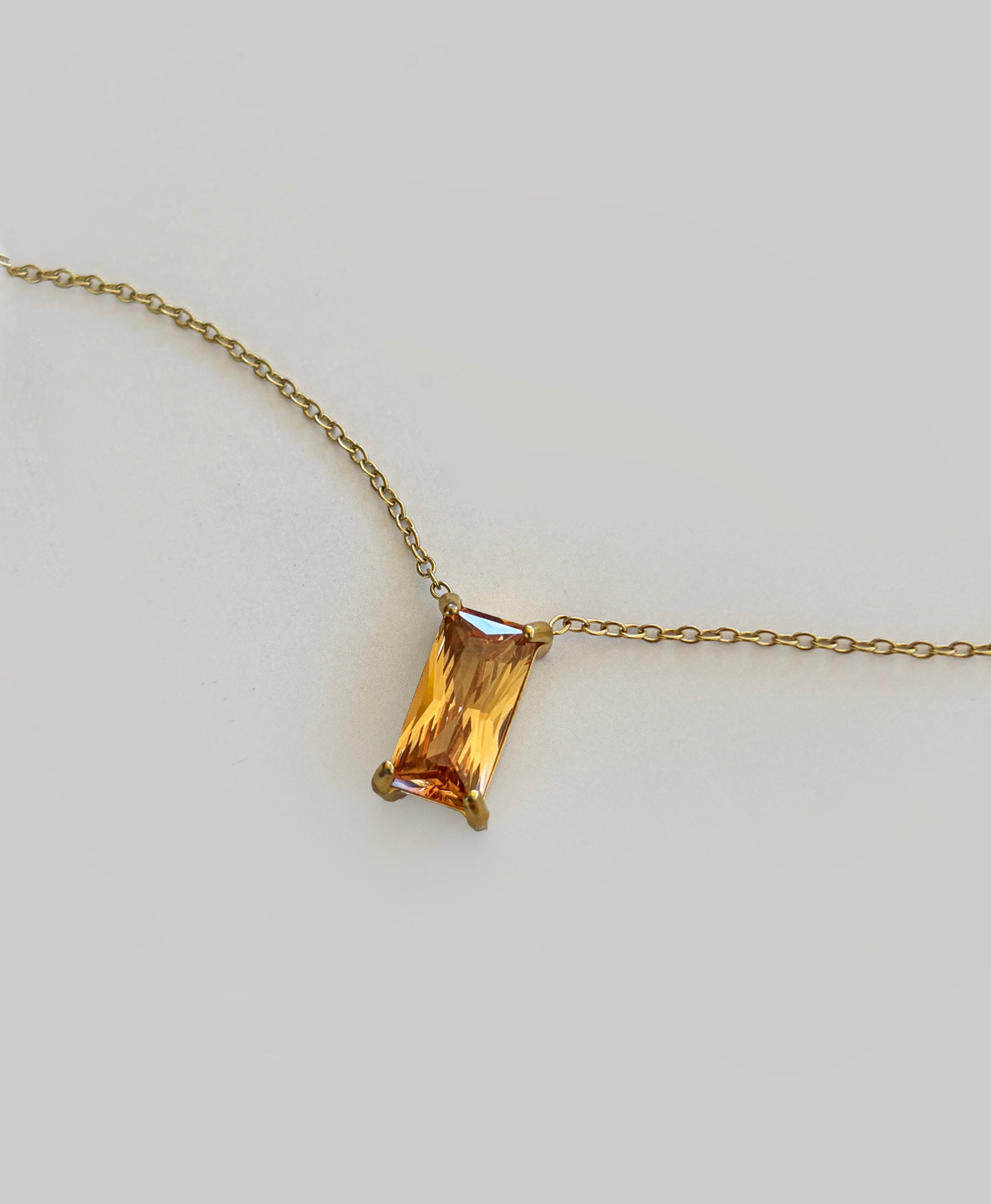 The Wild Honey Necklace by LLUME Jewelry features a rectangular, amber-colored gemstone pendant—reminiscent of honey—set in a simple gold prong setting, displayed against a light gray background.