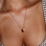 A close-up of a person’s chest wearing the Wild Honey Necklace by LLUME Jewelry, a dainty gold necklace with a rectangular pendant, styled with a brown and white checkered top. This everyday piece features waterproof craftsmanship for lasting shine.