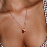 A close-up of a person’s chest wearing the Wild Honey Necklace by LLUME Jewelry, a dainty gold necklace with a rectangular pendant, styled with a brown and white checkered top. This everyday piece features waterproof craftsmanship for lasting shine.
