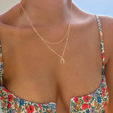A person wearing a colorful floral dress and LLUME Jewelry’s Wishbone Daily Set necklace is shown from shoulders to mid-chest, sunlight illuminating their skin.