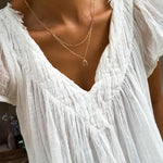 A person wears the Wishbone Daily Set by LLUME Jewelry with a sheer, white, textured V-neck blouse. The photo is cropped to show only the neck, chest, and upper torso.